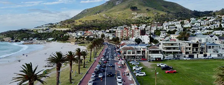Coastal road by beach leads to grand mountain.